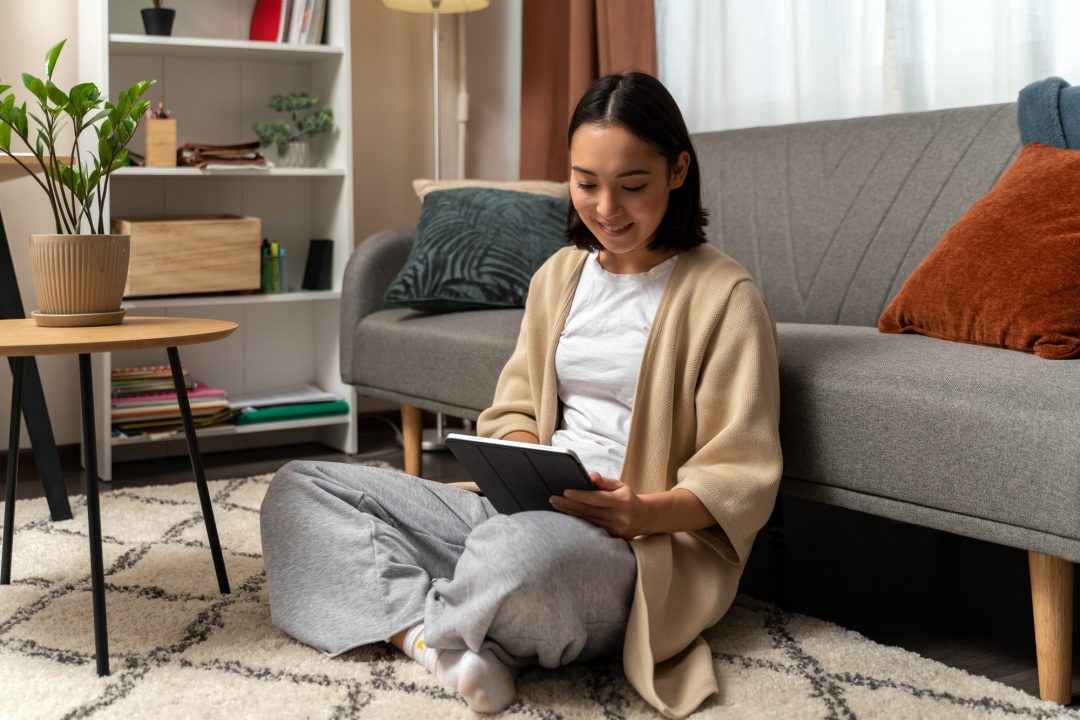 Happy young biracial female resting at home and using pad gadget while browsing web